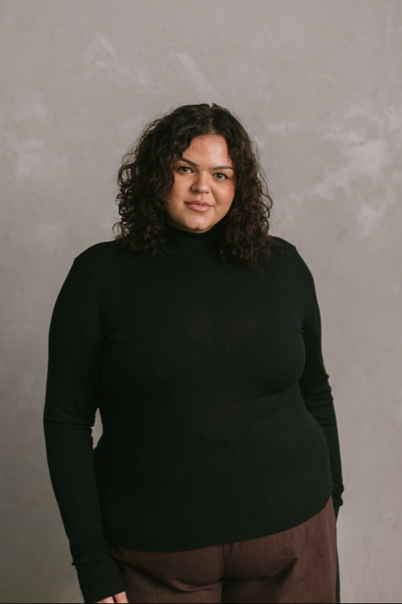 Person wearing a black turtleneck and brown pants against a gray background