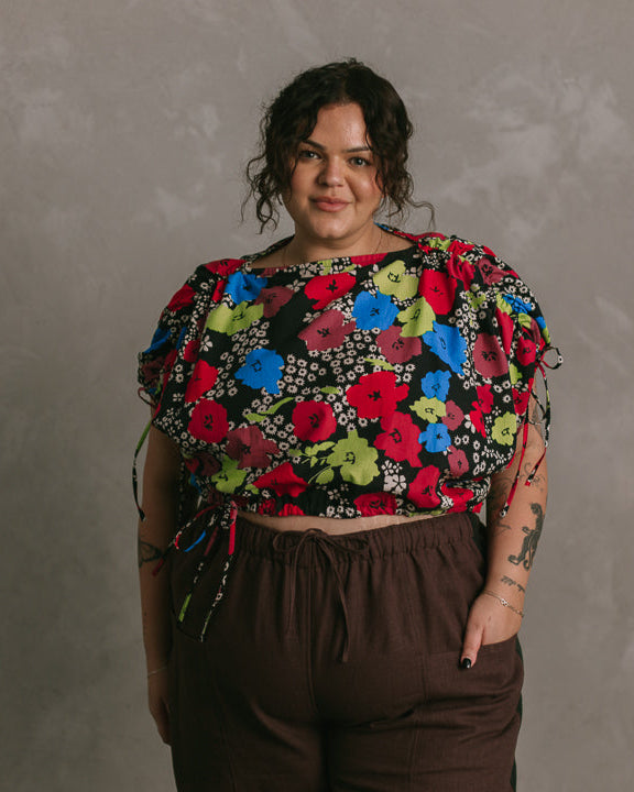 Person wearing a colorful floral top and brown pants against a gray background