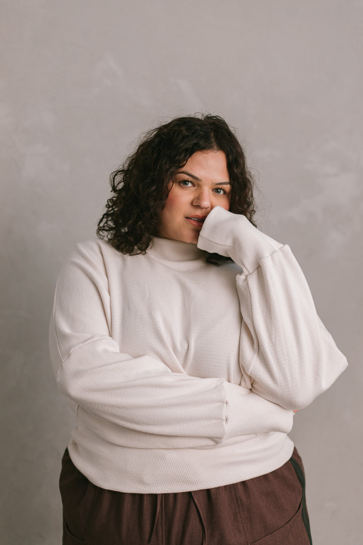 Person wearing a white sweater against a plain background