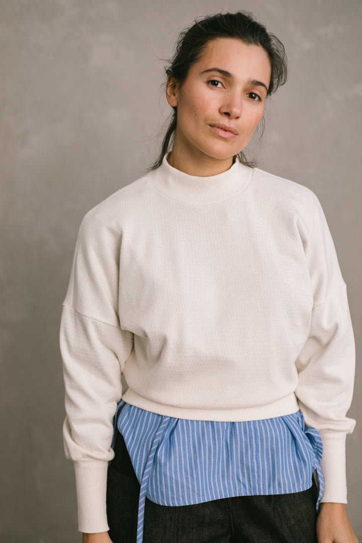 Woman wearing a white sweater over a blue shirt against a plain background