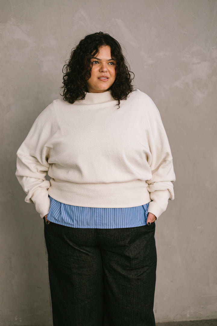 Woman wearing a white sweater over a blue shirt against a plain background