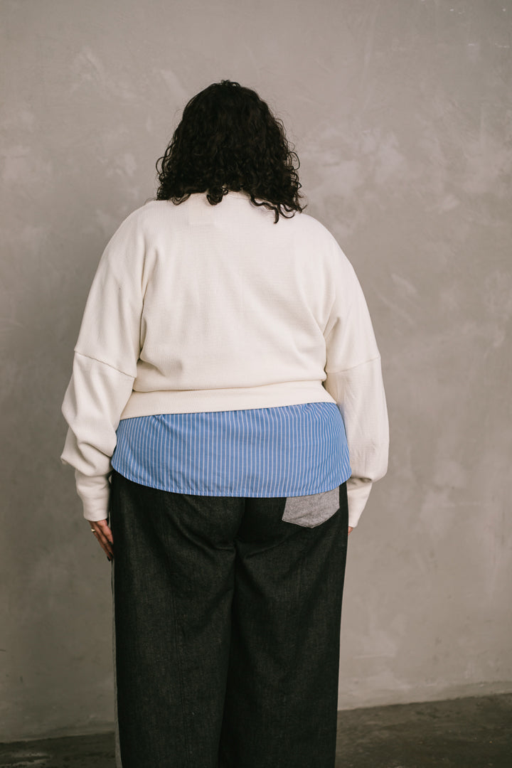Woman wearing a white sweater over a blue shirt against a plain background