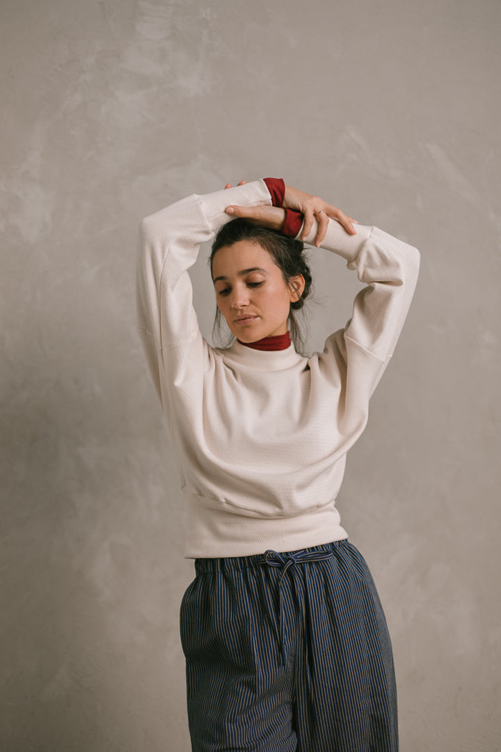 Woman wearing a white sweater over a red skivvy against a plain background