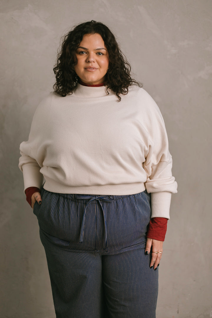 Person wearing a white sweater and blue striped pants against a plain background